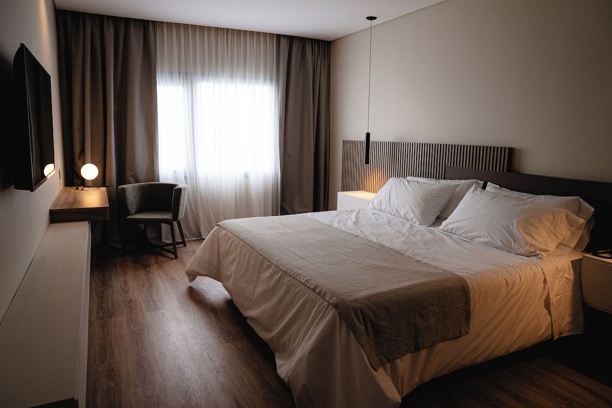 A hotel room with a bed, a desk with a lamp, a chair, and a television.