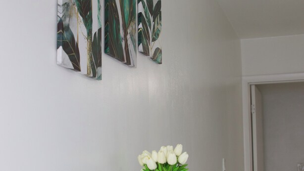 A room with a white table, a vase with white flowers, and three leaf-patterned wall art pieces. - Cozy Studio Near Hard Rock Stadium (Miami)