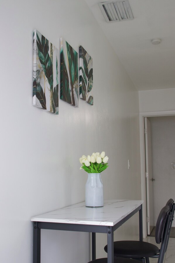 A room with a white table, a vase with white flowers, and three leaf-patterned wall art pieces.