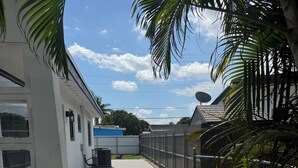A paved pathway leading to a white building with a satellite dish, surrounded by a chain-link fence and palm trees. - Cozy Studio Near Hard Rock Stadium (Miami)
