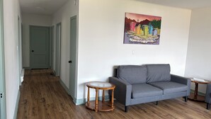 A living room with a grey sofa, two round wooden side tables, and a painting of colorful houses on the wall.