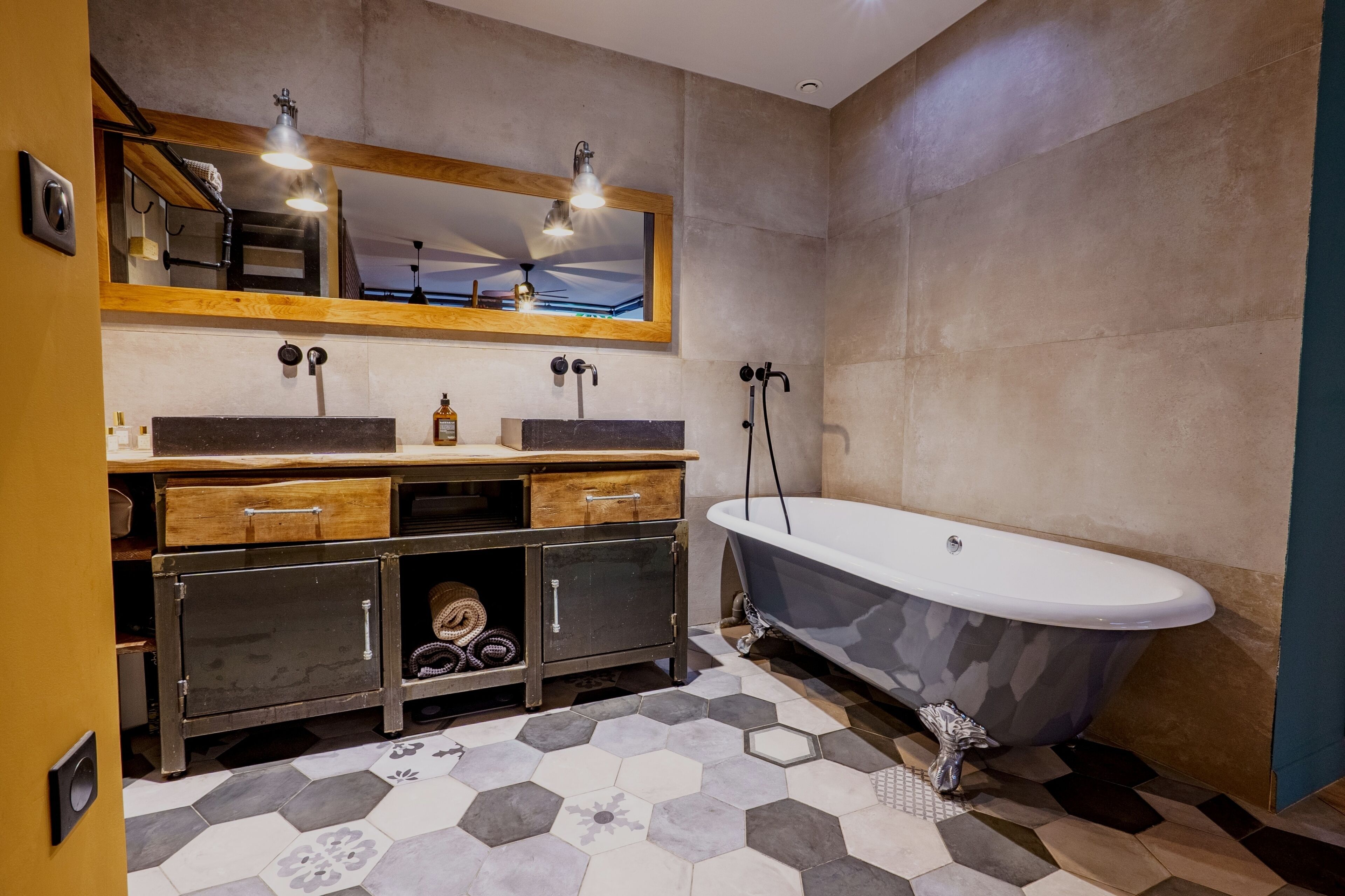 Une salle de bain avec une baignoire sur pieds, un meuble-lavabo en bois doté de tiroirs, un grand miroir et des carreaux à motifs hexagonaux.