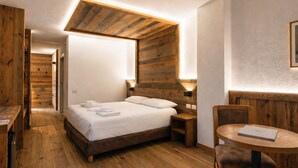 A wooden-floored room with a bed, bedside table, and a round table with chairs. - Hotel Soran (San Lorenzo Dorsino)