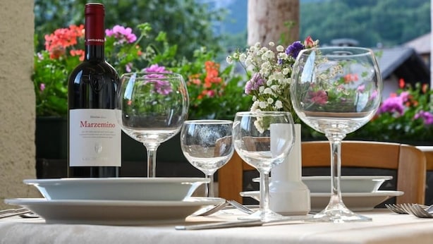 A table set with wine glasses, a bottle of Marzemino wine, and a vase with flowers. - Hotel Soran (San Lorenzo Dorsino)