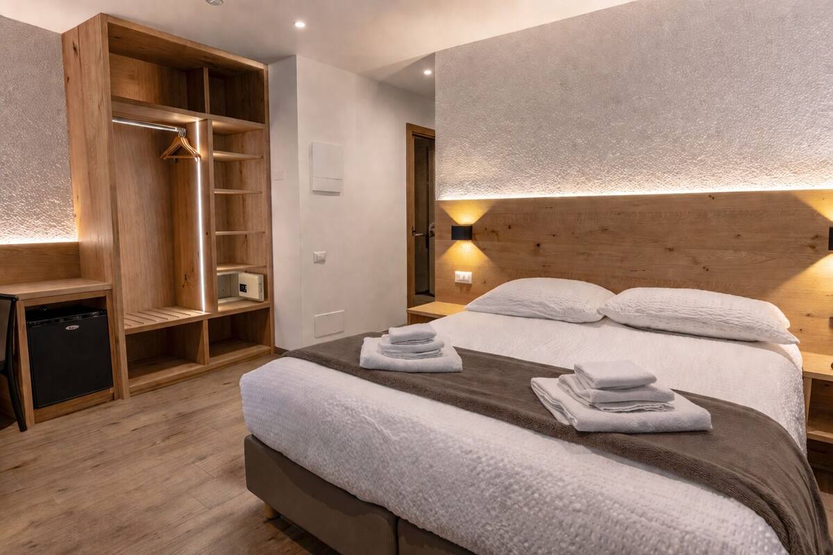 Un dormitorio con cama, un armario de madera, una mesita de noche y una lámpara de pared.