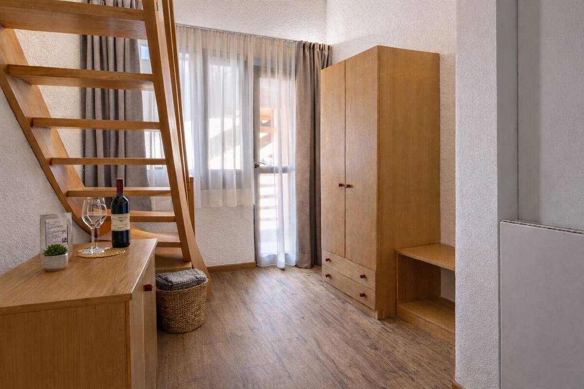 Una habitación con un escritorio de madera, una botella de vino, una copa de vino, una escalera y un armario.