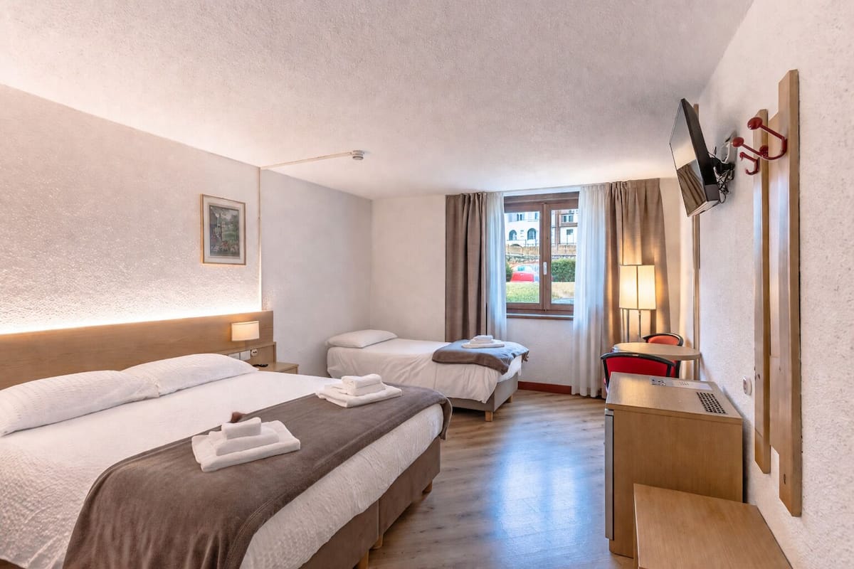 Habitación de hotel con dos camas, un escritorio, televisor y ventana con cortinas.