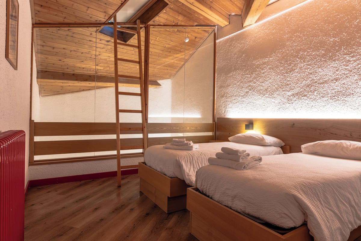 Un dormitorio con techo estilo loft, suelo de madera y una escalera que lleva al espacio para dormir superior.