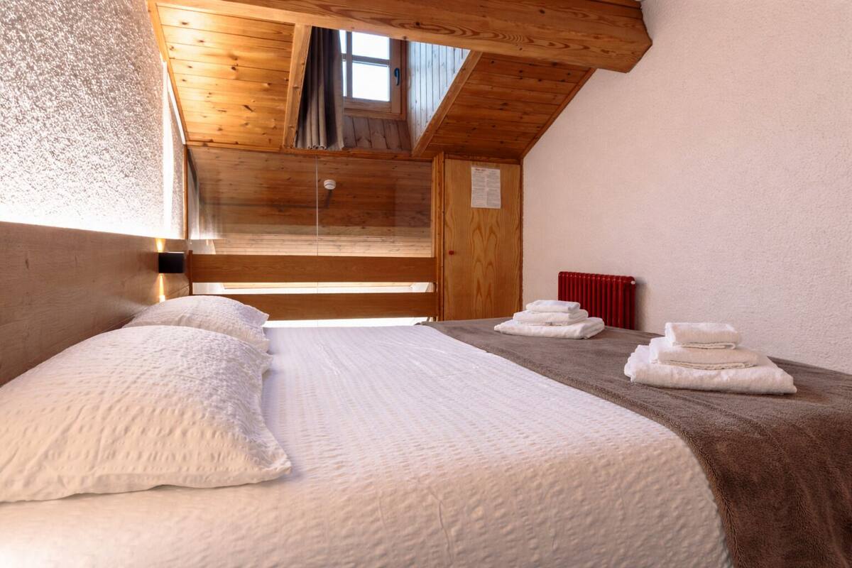 Una habitación con una cama, una ventana, un radiador rojo y un techo de madera.