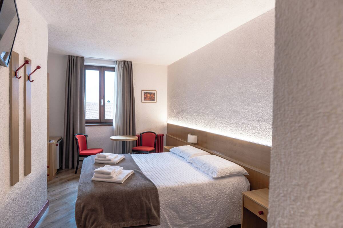 Una habitación de hotel con cama, escritorio, silla y ventana.