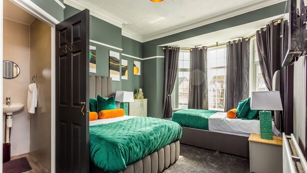 Ein Schlafzimmer mit zwei Betten, einem Nachttisch, einer Lampe, einem Spiegel und Blick ins Freie.