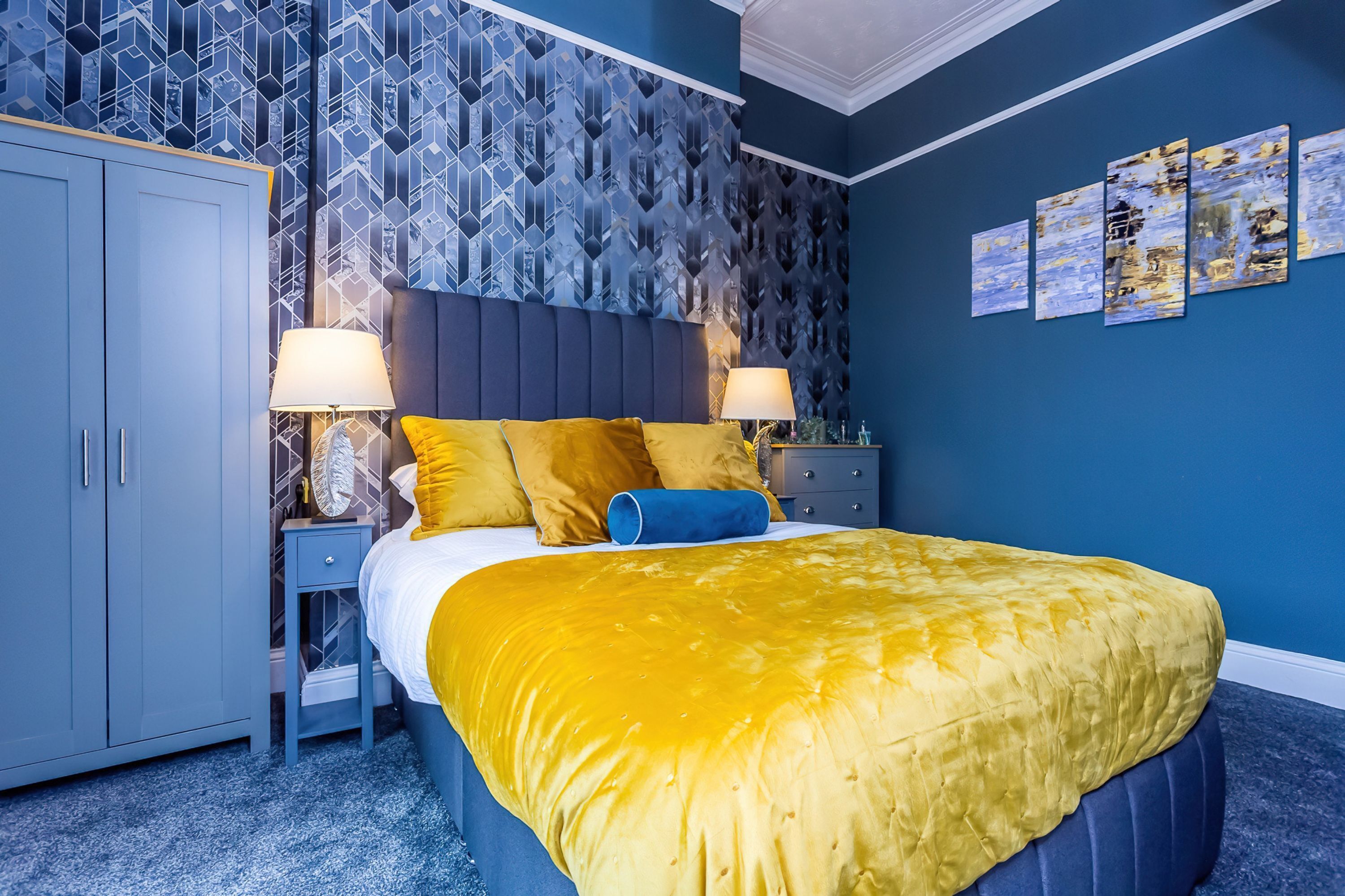Une chambre à coucher avec un lit, des tables de chevet, une armoire et un mur décoré d’un motif.