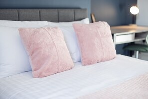A bed with white bedding and two pink pillows, a grey headboard, and a bedside table with a lamp. - Anika in South Shields (South Shields)