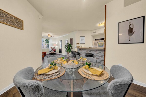 Un coin repas avec une table en verre, des chaises à revêtement gris et une cuisine en arrière-plan.