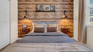 A bedroom with a wooden wall, a bed with pillows, two bedside tables, a clock, and a framed picture. - Modern 2BR 2BA w King Bed Pools Gym 1 (Tampa)