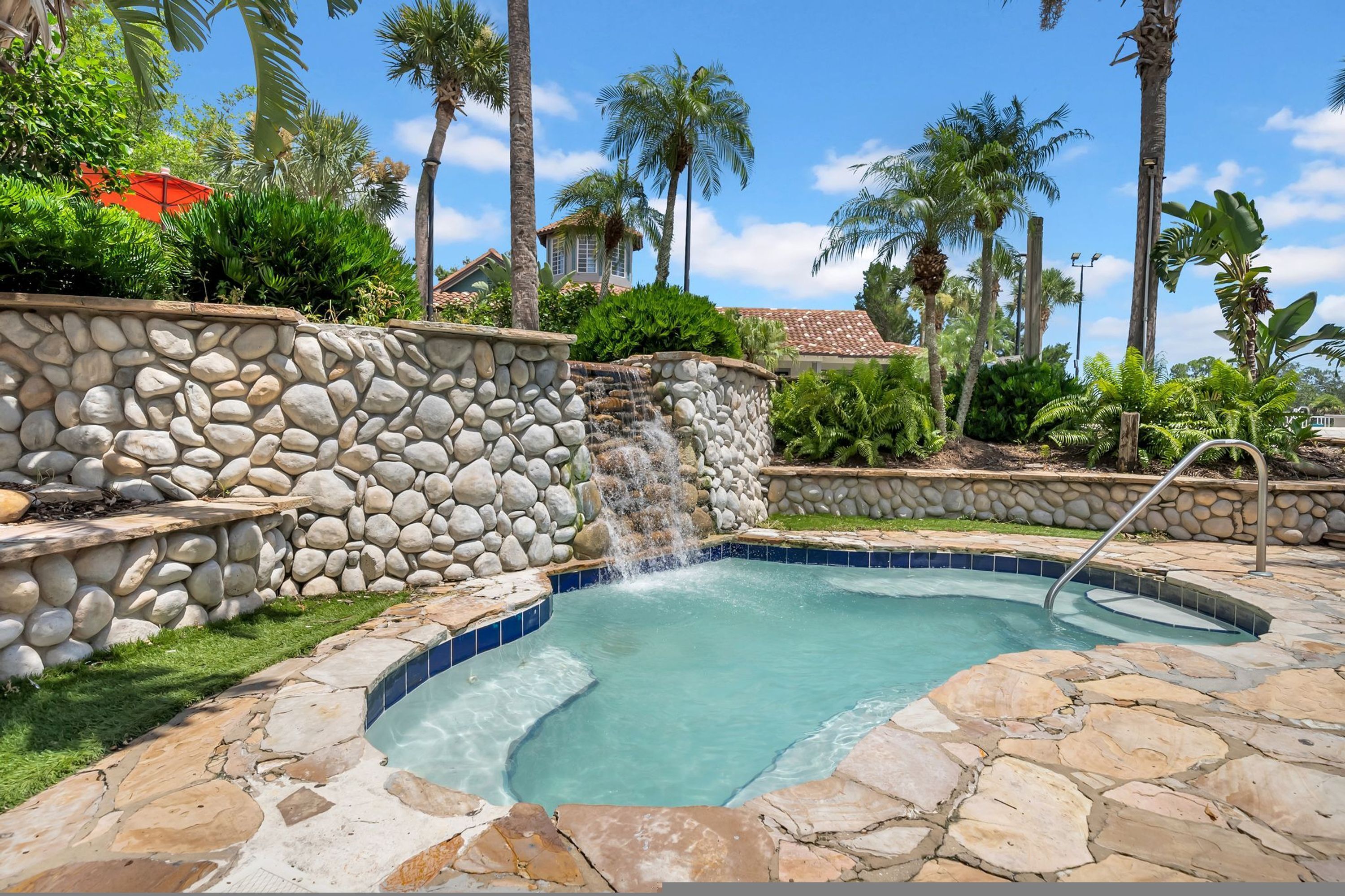A stone-walled pool with a waterfall feature, surrounded by palm trees and a stone deck.