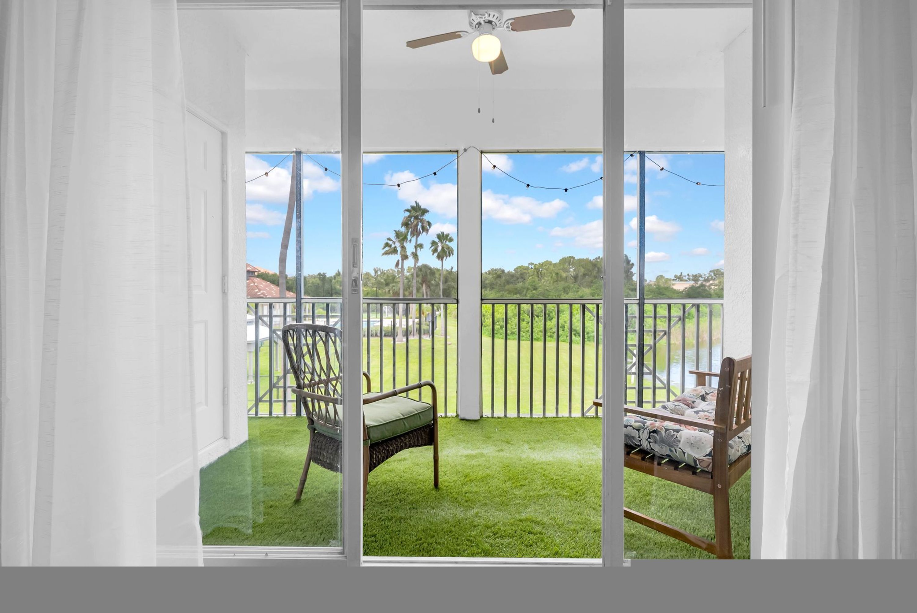 A room with a sliding glass door leading to a balcony with a view of palm trees and a grassy area.