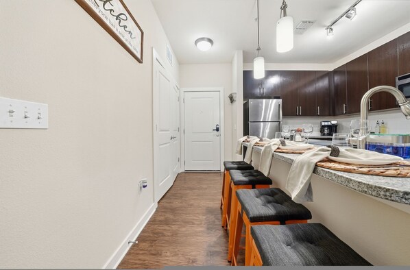 A modern kitchen with a stainless steel refrigerator, a built-in oven, and a microwave. There are wooden stools and a countertop with a sink. - Stylish 2BR w Pool Pet-friendly Unit 13 (Tampa)