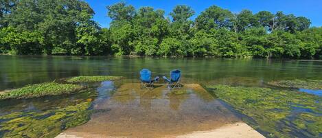 A clear river with two blue chairs on a wooden dock.