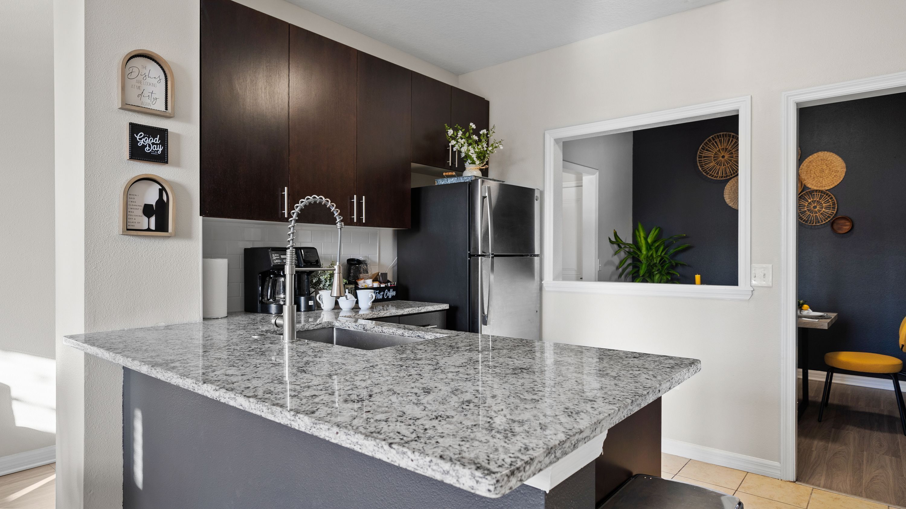 Una cocina moderna con armarios de madera oscura, un refrigerador de acero inoxidable, encimera de granito y una cafetera.