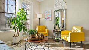 A living room with two yellow armchairs, a wooden coffee table, a potted plant, a floor lamp, and a mirror. - Stylish 2BR Corporate Stay Pool Balcony 2 (Tampa)