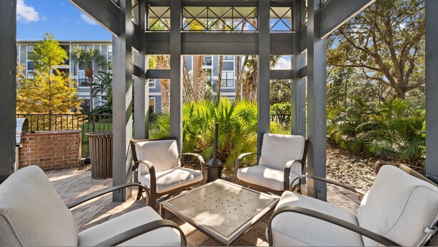 A covered outdoor seating area with chairs and a table, surrounded by greenery and a view of buildings. - Stylish 2BR Corporate Stay Pool Balcony 2 (Tampa)