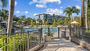 A resort with a swimming pool, lounge chairs, palm trees, and a building in the background. - Stylish 2BR Corporate Stay Pool Balcony 2 (Tampa)