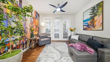 A living room with a gray sofa, a coffee table, a ceiling fan, a large abstract painting, and a potted plant.