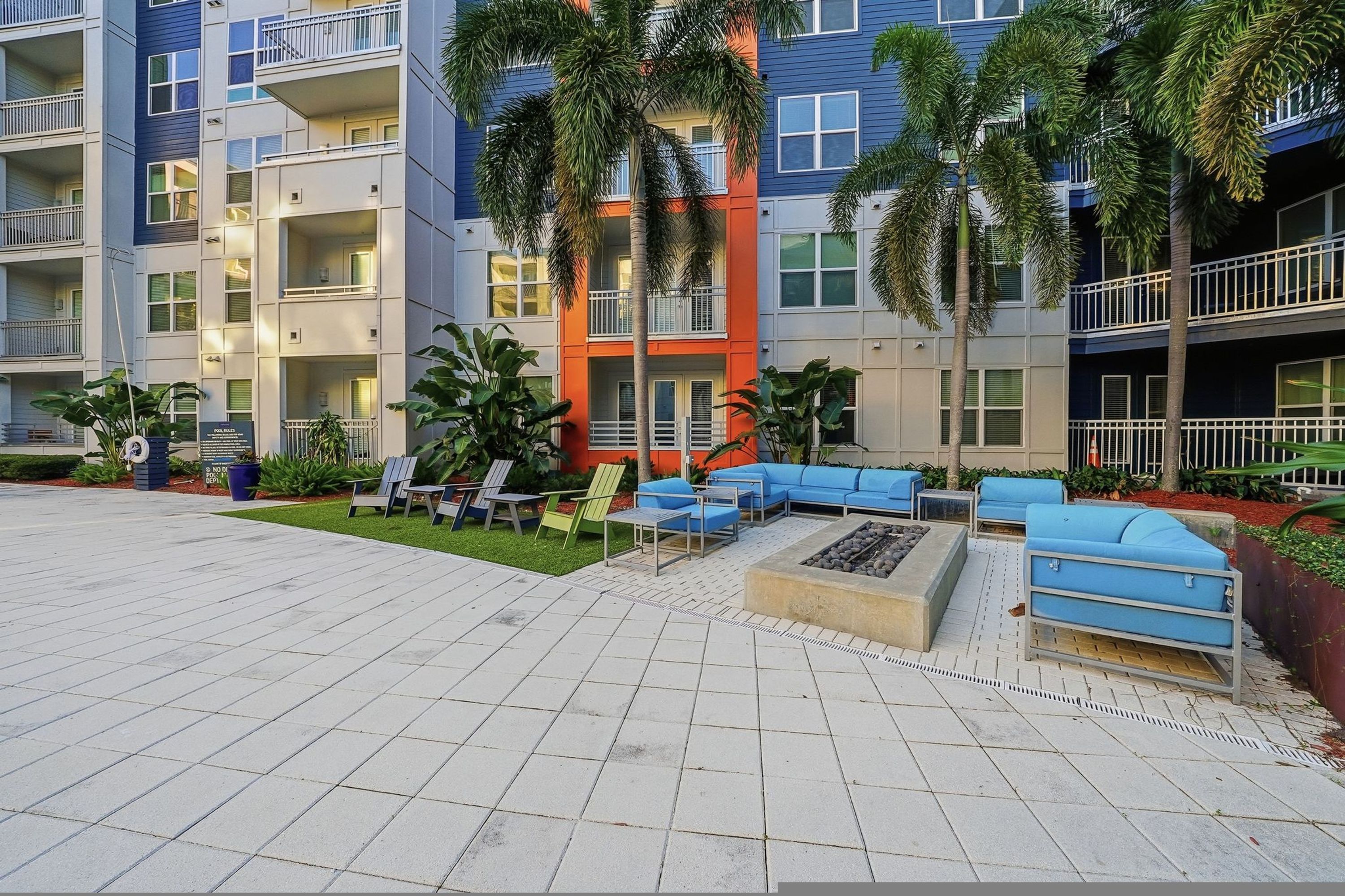 A multi-story residential building with balconies, outdoor seating, and palm trees.