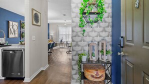 A modern kitchen with a dishwasher, a dining area with chairs and a table, and a hallway with a patterned wall and a door. - Stylish 2BR 2BA w Pool Gym Near Airport 3 (Tampa)