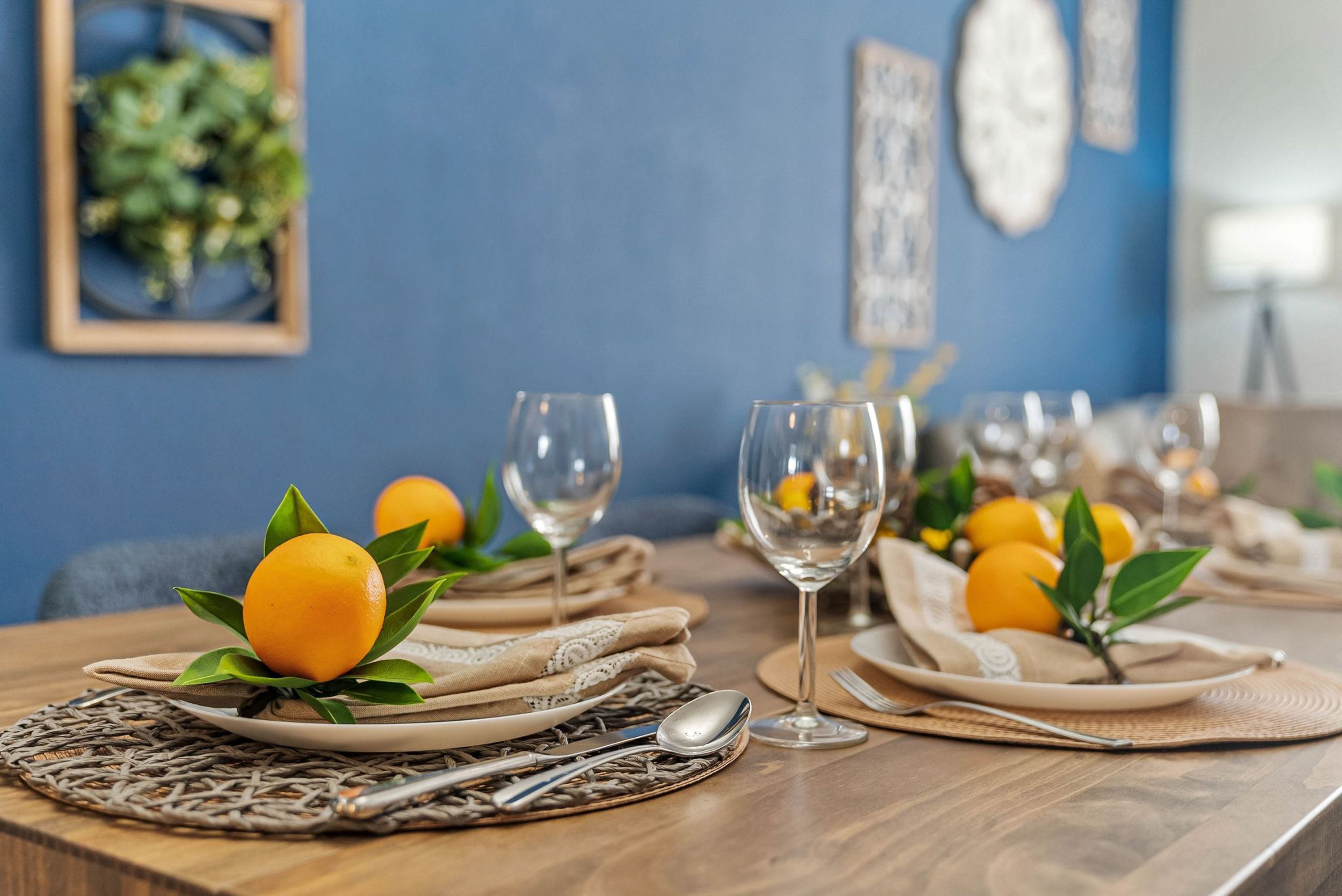 Une table à manger dressée avec des assiettes, des verres et des feuilles d’automne aux couleurs orangées.