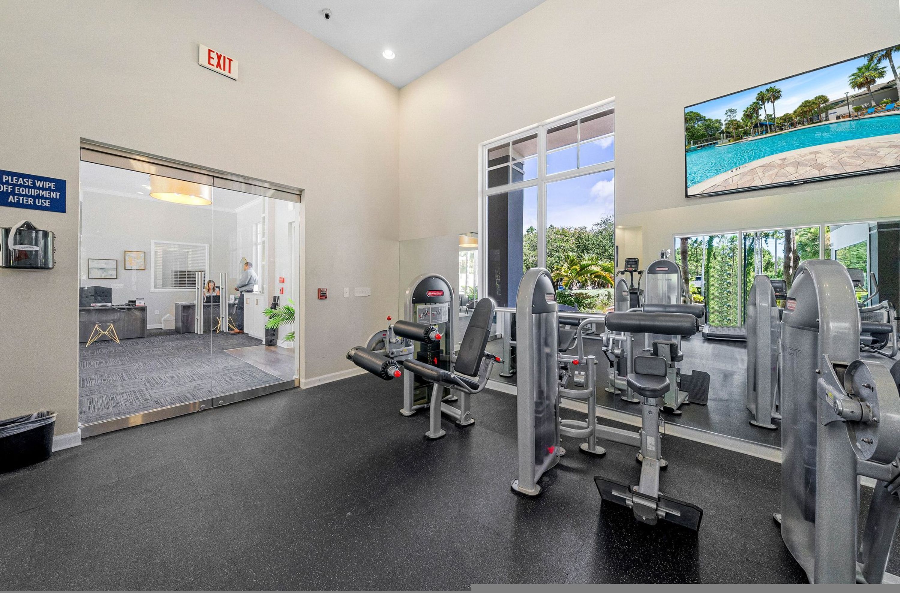 A gym with exercise equipment, a large window, and an exit sign.