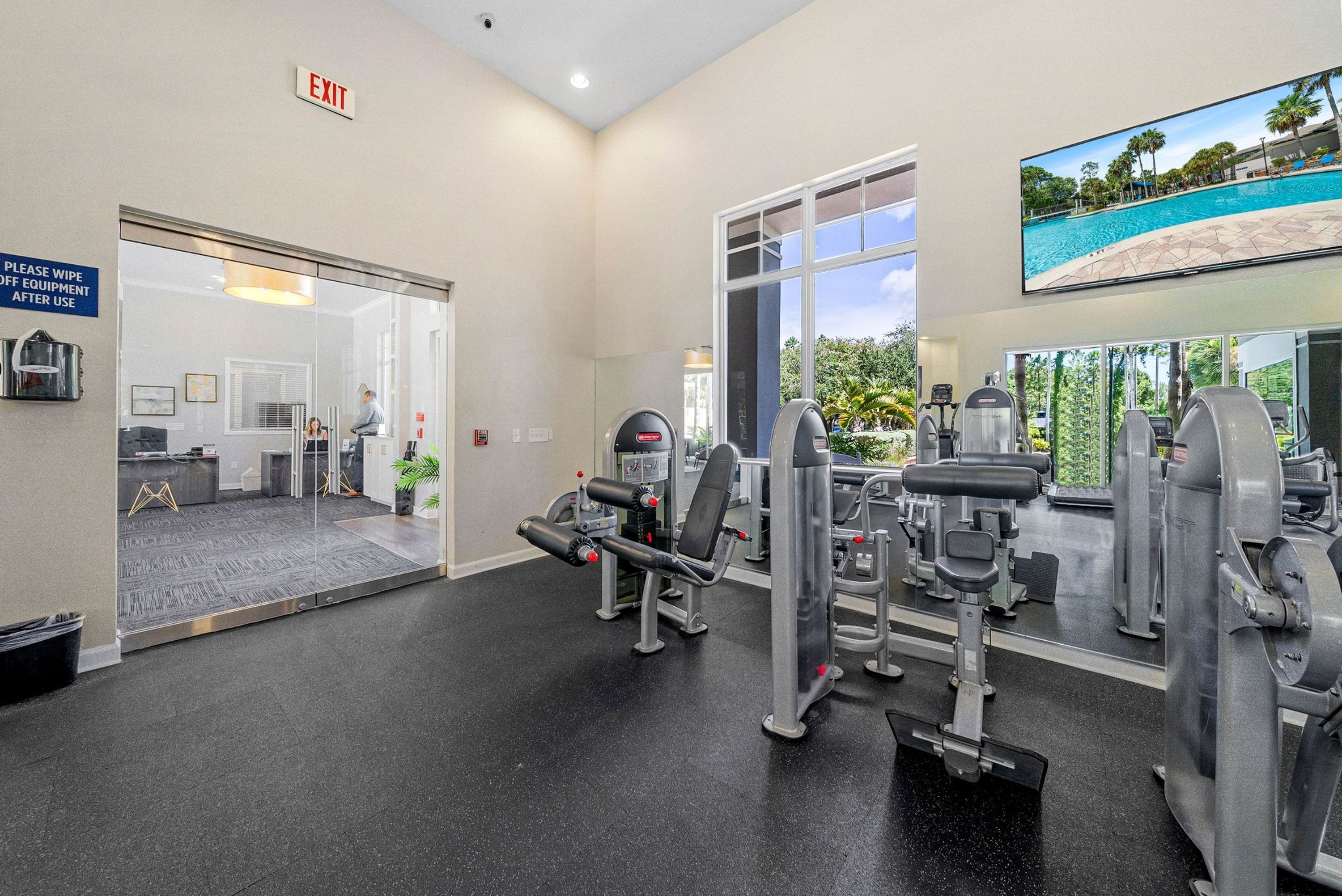 Un gimnasio con equipo de ejercicio, una zona de recepción y un amplio ventanal con vistas a zonas verdes.