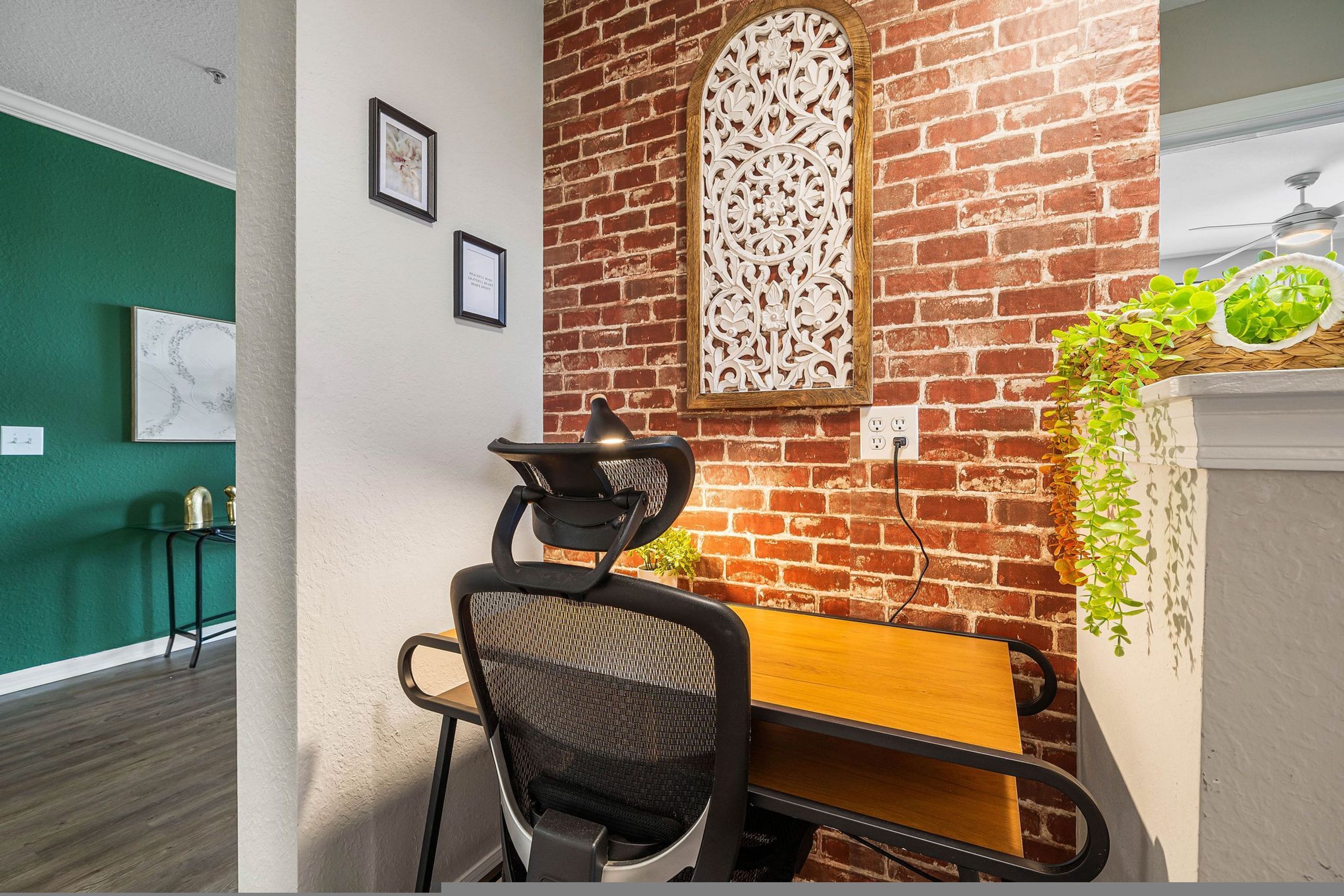 A conference room with a brick wall, a wooden table, a black office chair, and a decorative wall piece.
