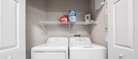 A laundry room with two front-loading washing machines, a shelf with detergent bottles, and a control panel.