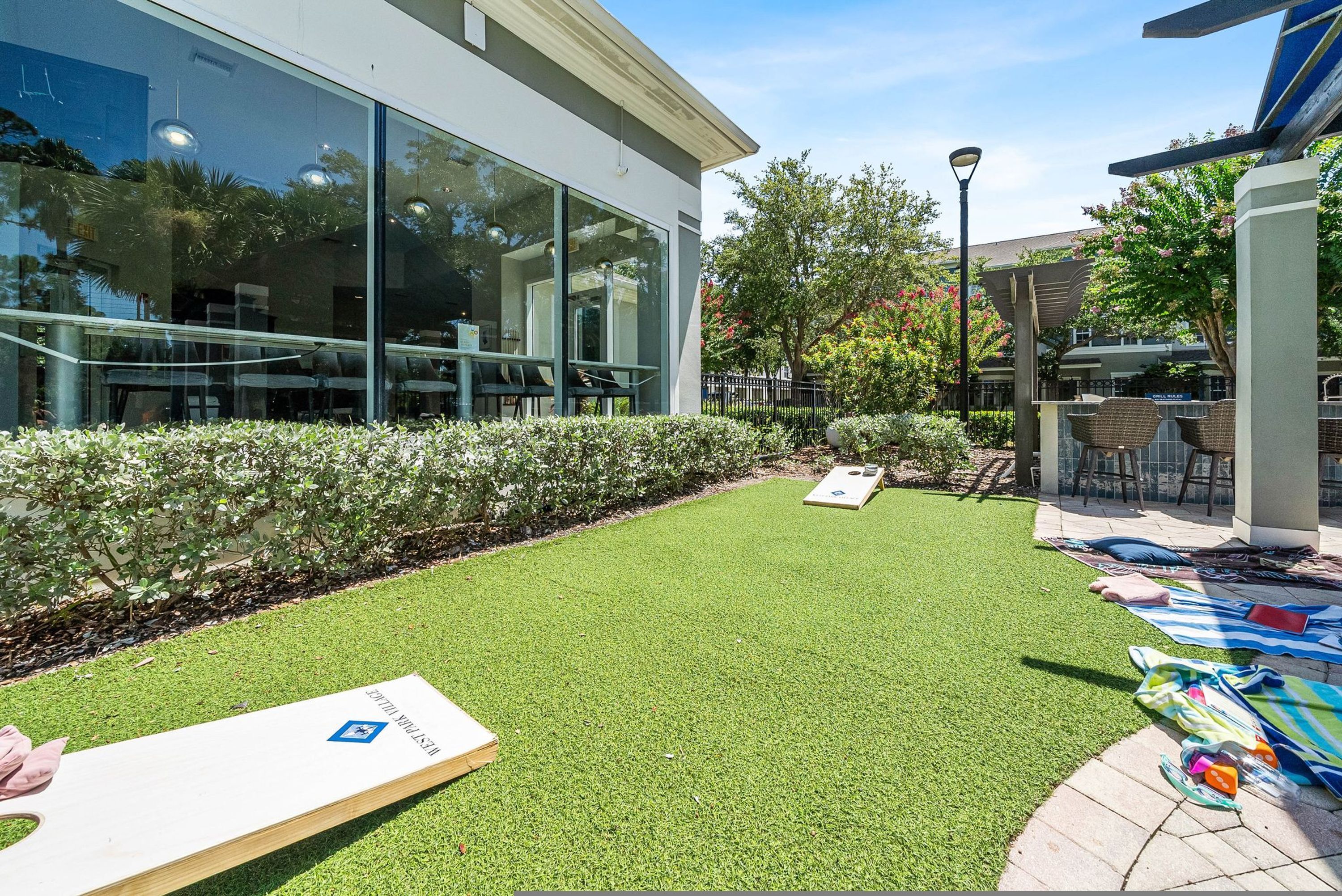 A modern building with large glass windows, a well-maintained lawn, outdoor seating, and a lamp post.