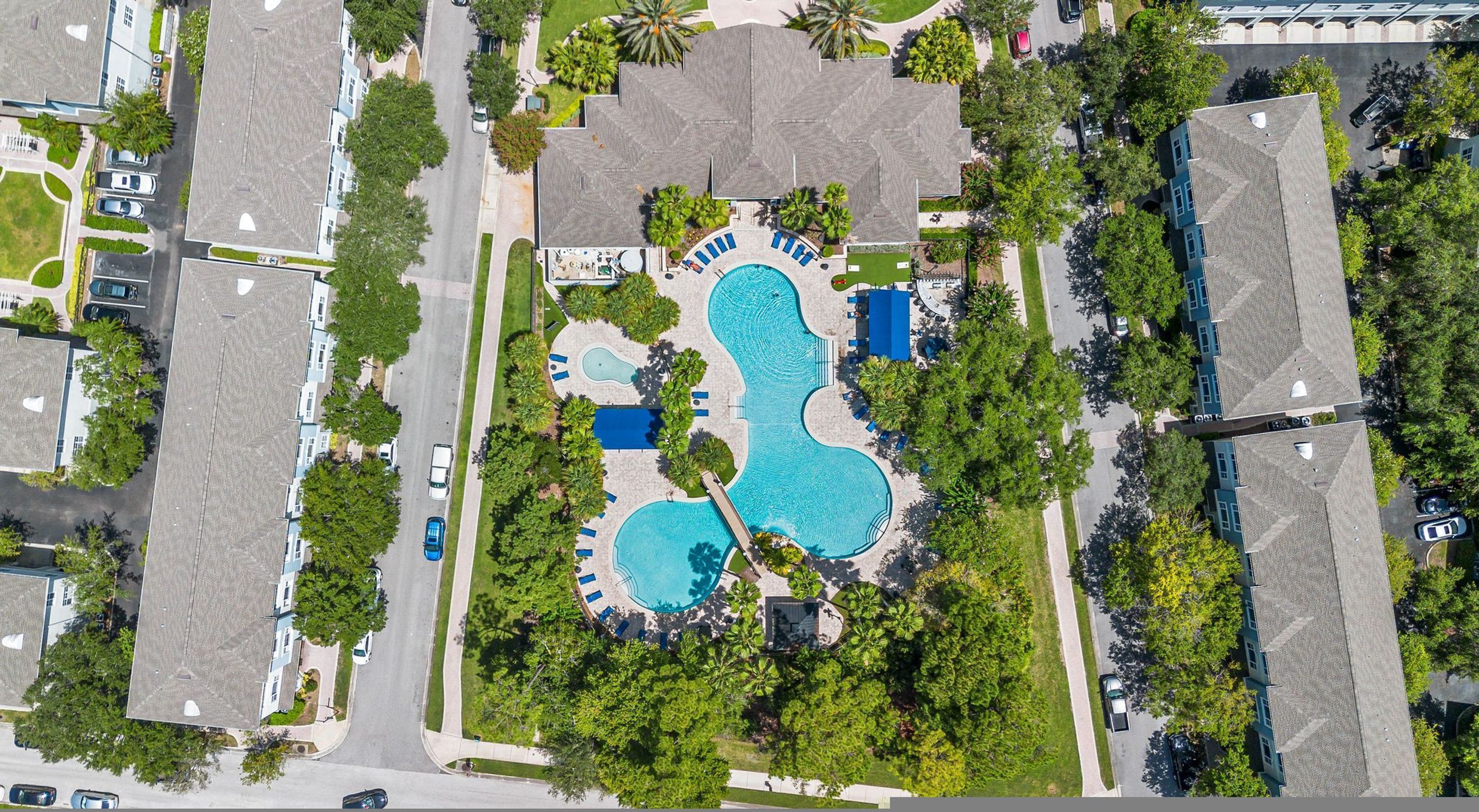 An aerial view of a residential area with a swimming pool, houses, and a road.
