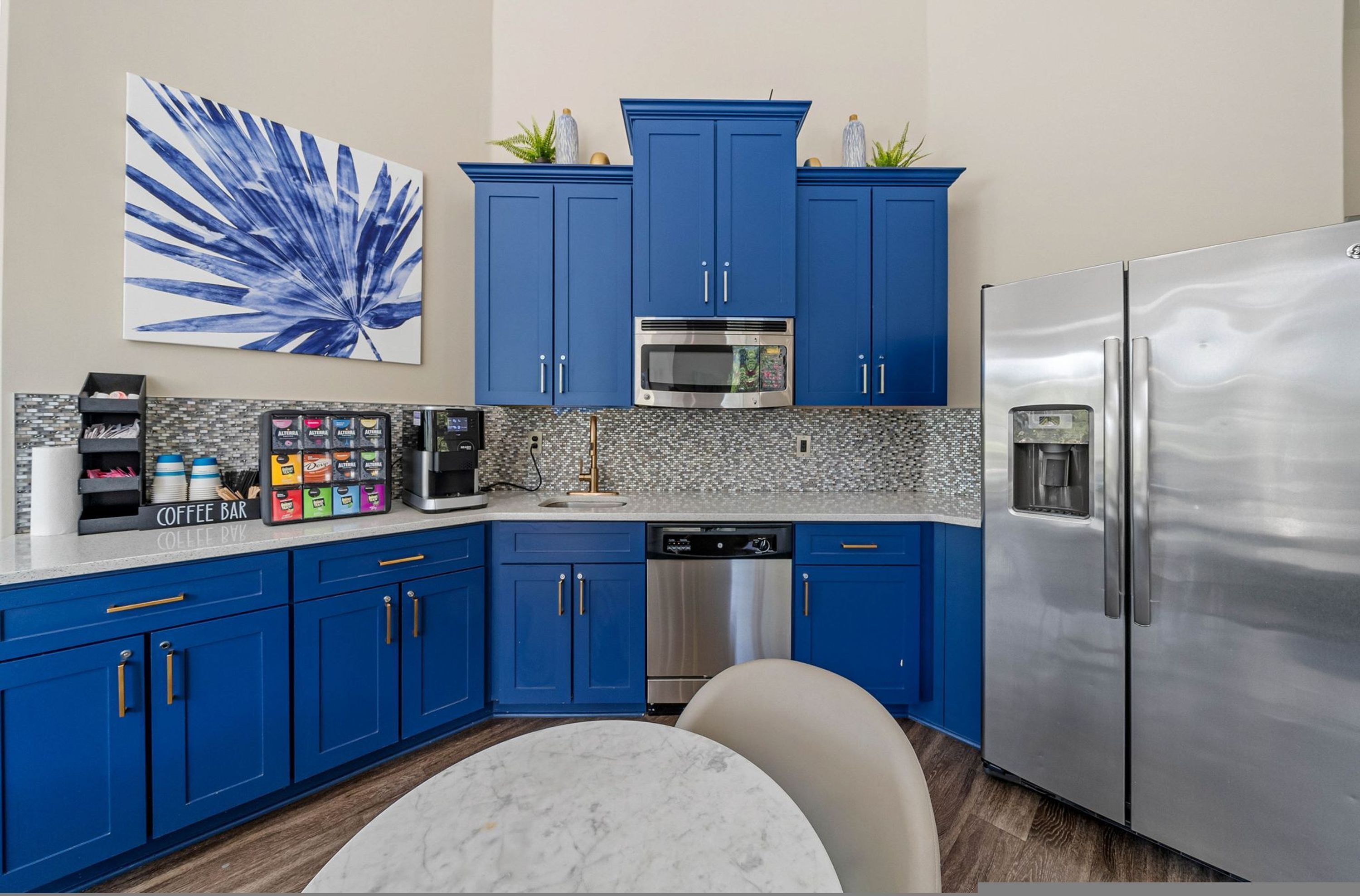 A kitchen with blue cabinets, a stainless steel refrigerator, a microwave, and a dishwasher.