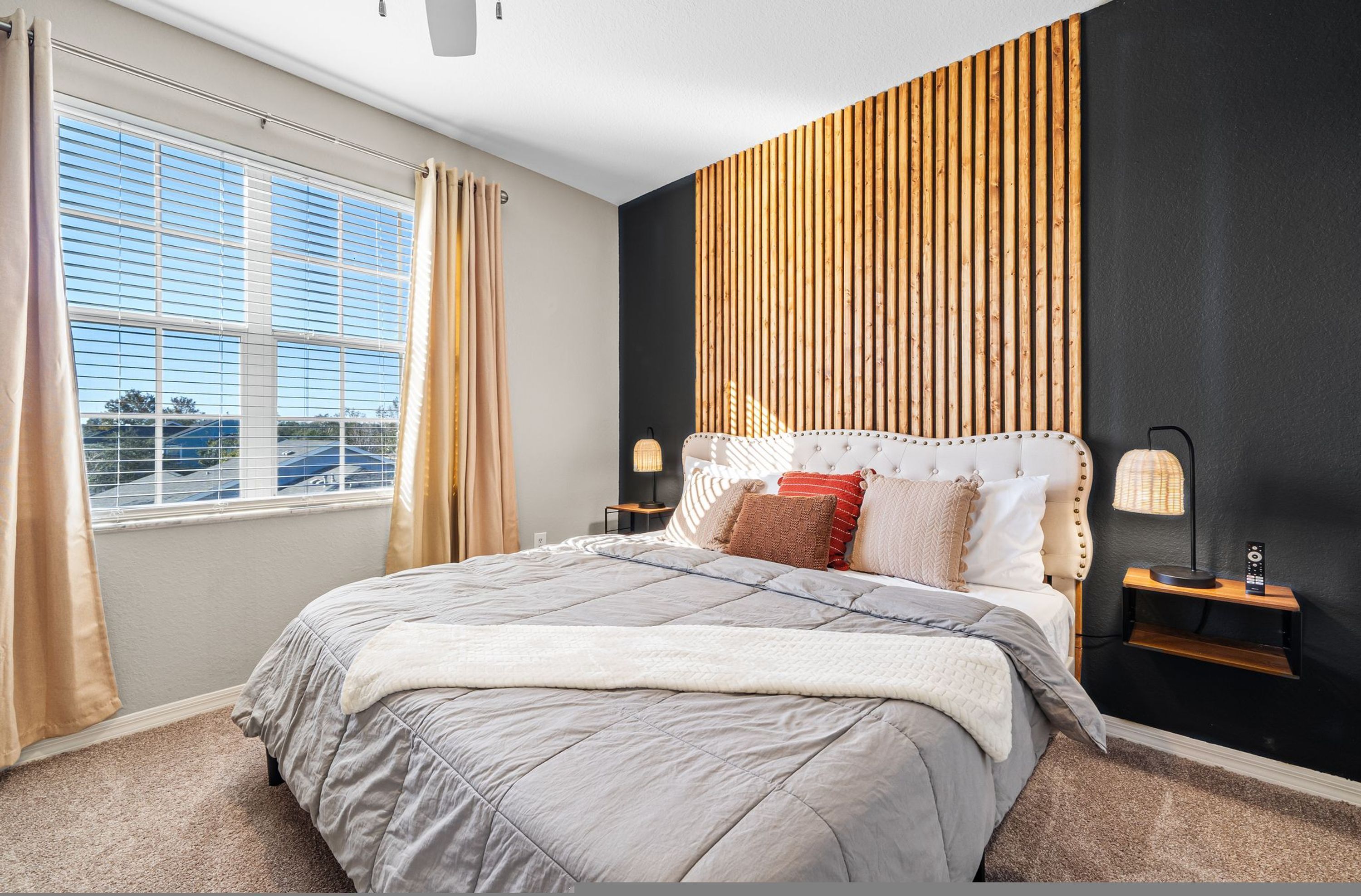 Ein Schlafzimmer mit einem großen Bett, einem Fenster mit Vorhängen, einer Wandlampe und einem Nachttisch.