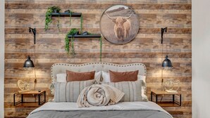 Quarto com parede de madeira, cama com cabeceira, mesas de cabeceira e prateleiras fixadas na parede com plantas.