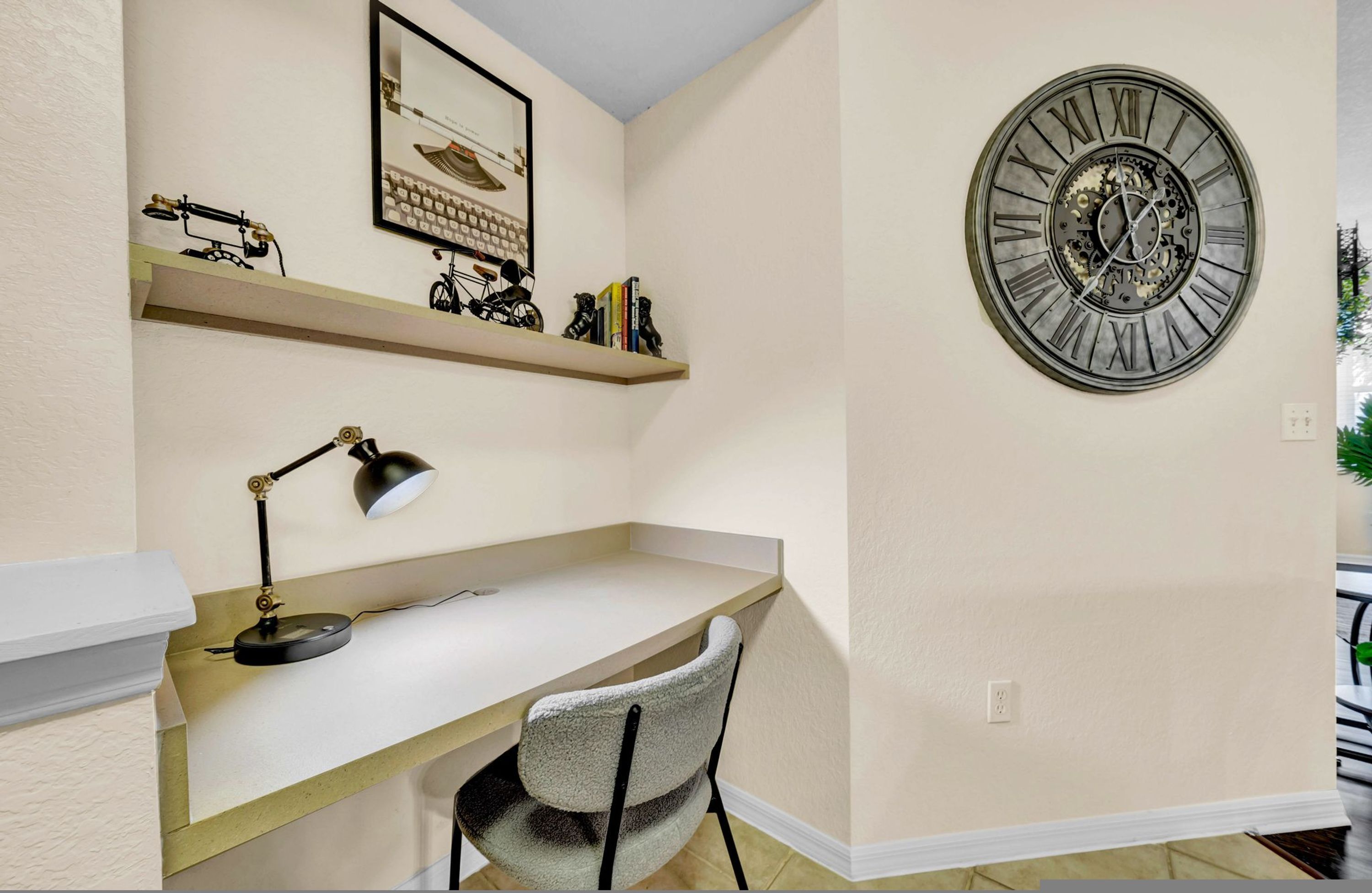 A corner room with a desk, chair, mounted clock, and shelves with decorative items.
