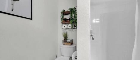 A bathroom with a toilet, a shower, and a wall-mounted shelf with plants.