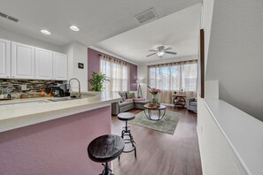 Cozinha moderna com armários brancos, área de bar e espaço de jantar com mesa redonda e banquetas.