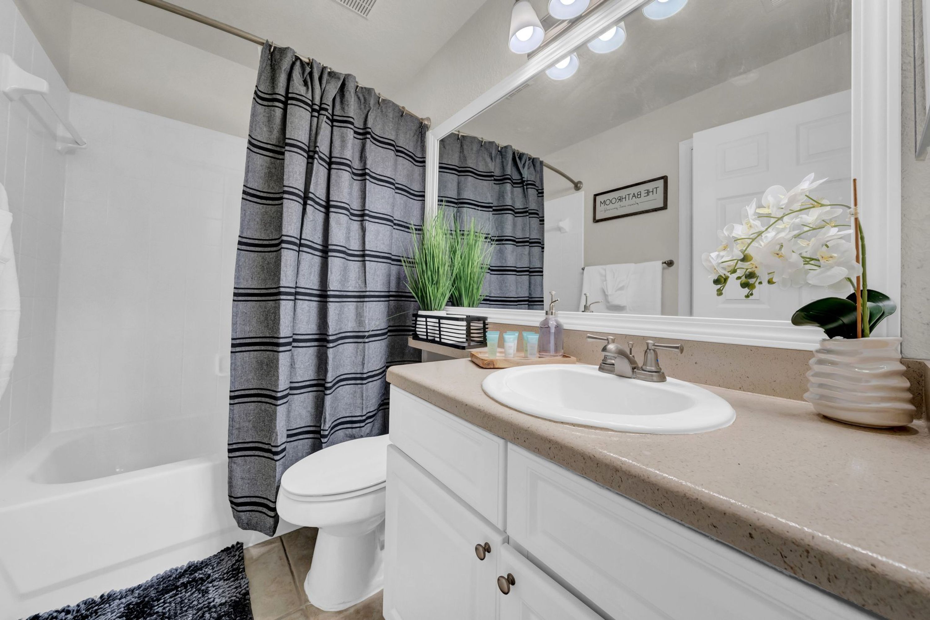 Un baño con inodoro blanco, un lavabo con espejo, cortina de ducha a rayas y una planta en maceta.