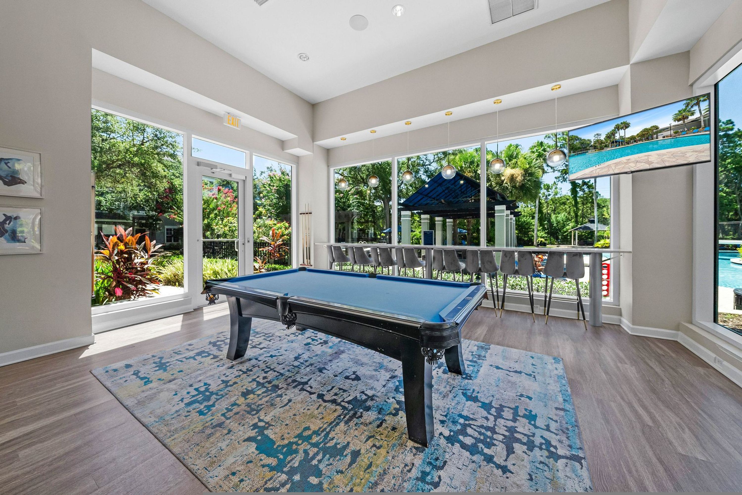 A pool table in a spacious room with large windows, a view of a pool, and a gazebo outside.