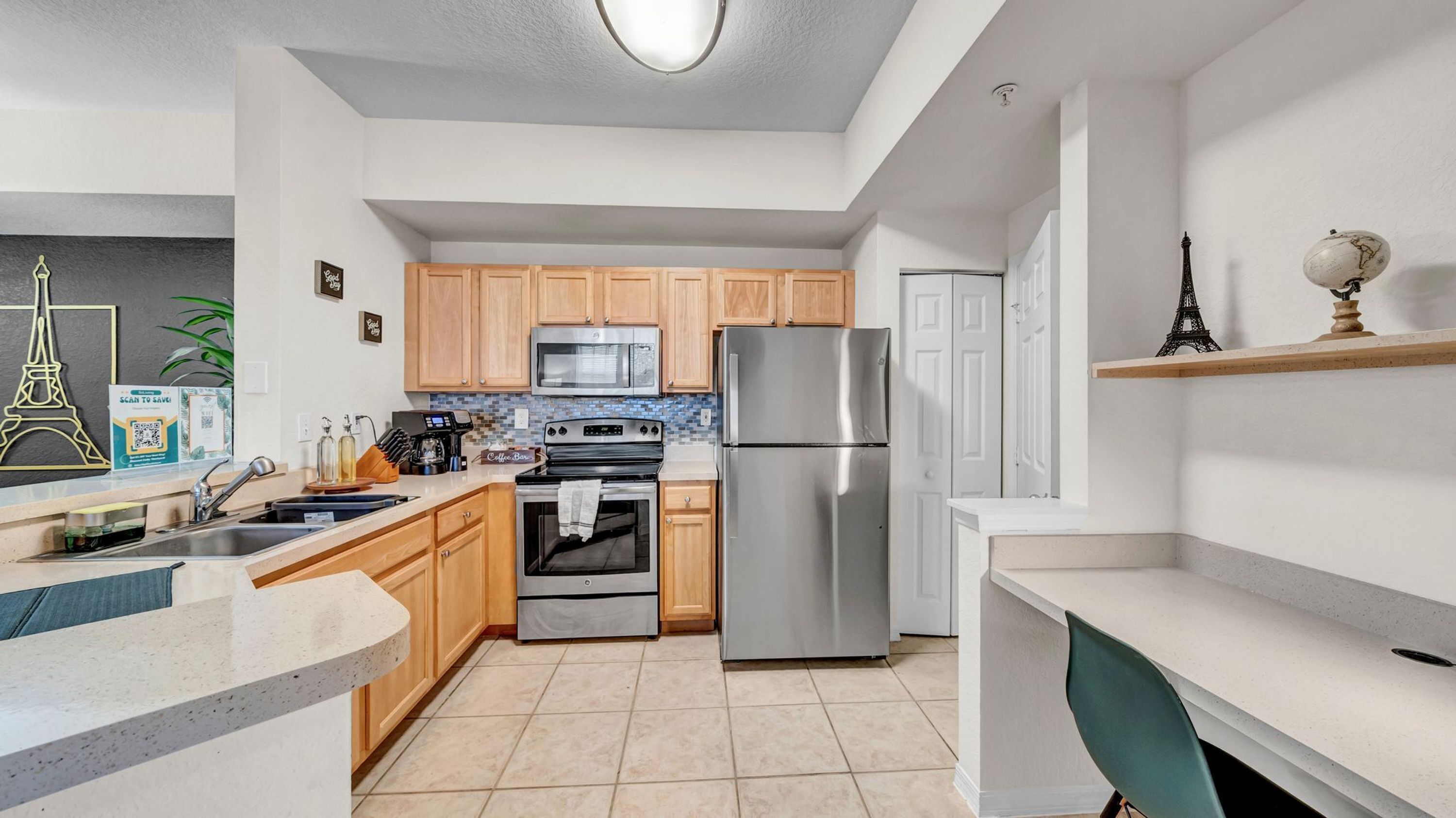 A modern kitchen with wooden cabinets, stainless steel appliances, a tiled backsplash, and a small Eiffel Tower decoration.