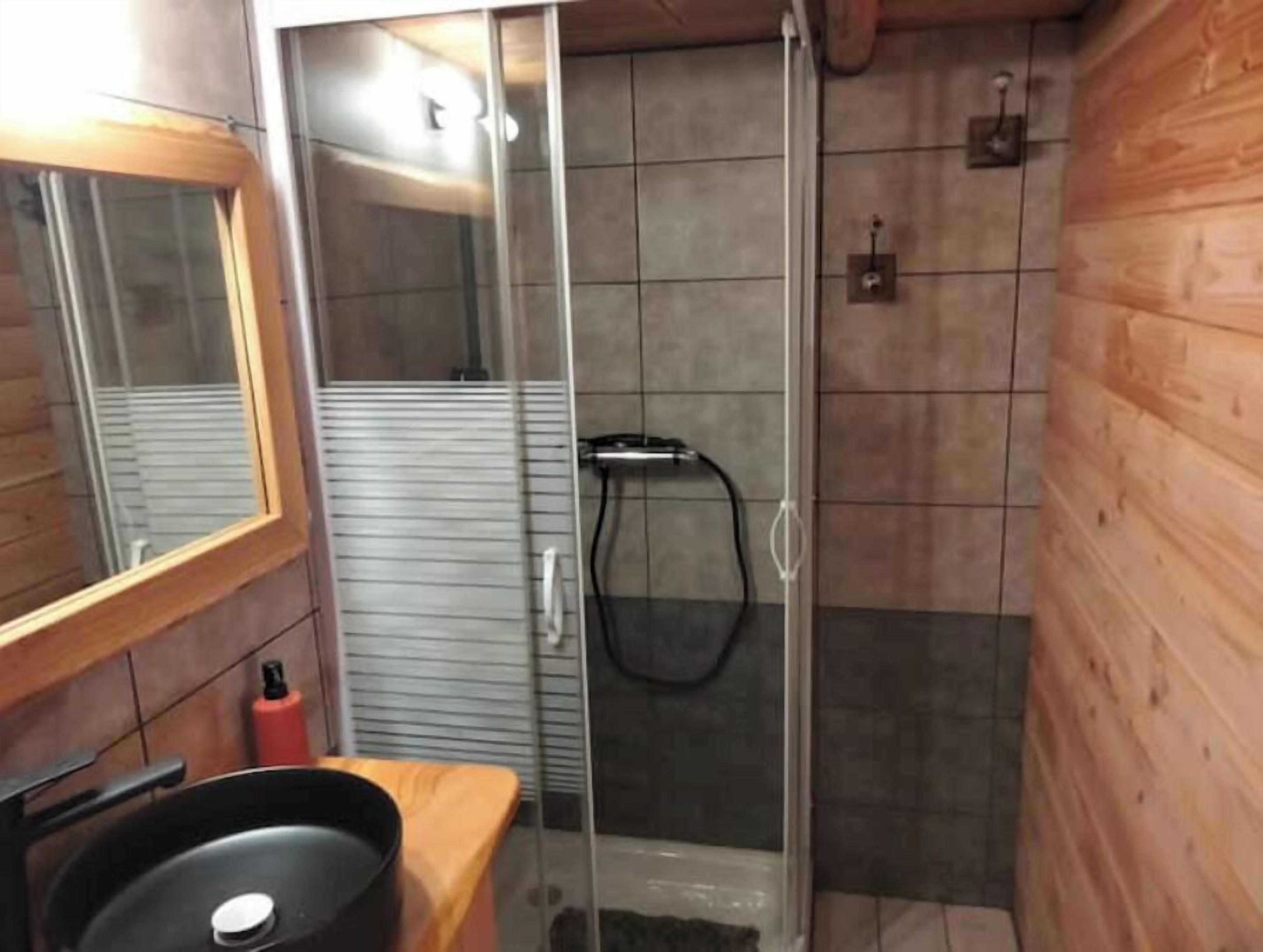 Une salle de bain avec un meuble-lavabo en bois, un miroir, un espace douche et des murs carrelés.