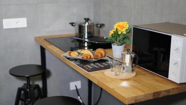 A kitchen with a microwave, a pot on the stove, a tray of croissants, a flower vase, and two stools. - Farina Rooms & Apartments - Hospitality with a View and Comfort in the City (San Nicola La Strada)
