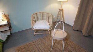A room with a wicker chair, a small round table, a lamp, and a bed with a green blanket. - Farina Rooms & Apartments - Hospitality with a View and Comfort in the City (San Nicola La Strada)