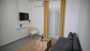 A modern living room with a sofa, a television, a wicker chair, a small wooden table with a bottle and glasses, and a window with curtains. - Farina Rooms & Apartments - Hospitality with a View and Comfort in the City (San Nicola La Strada)